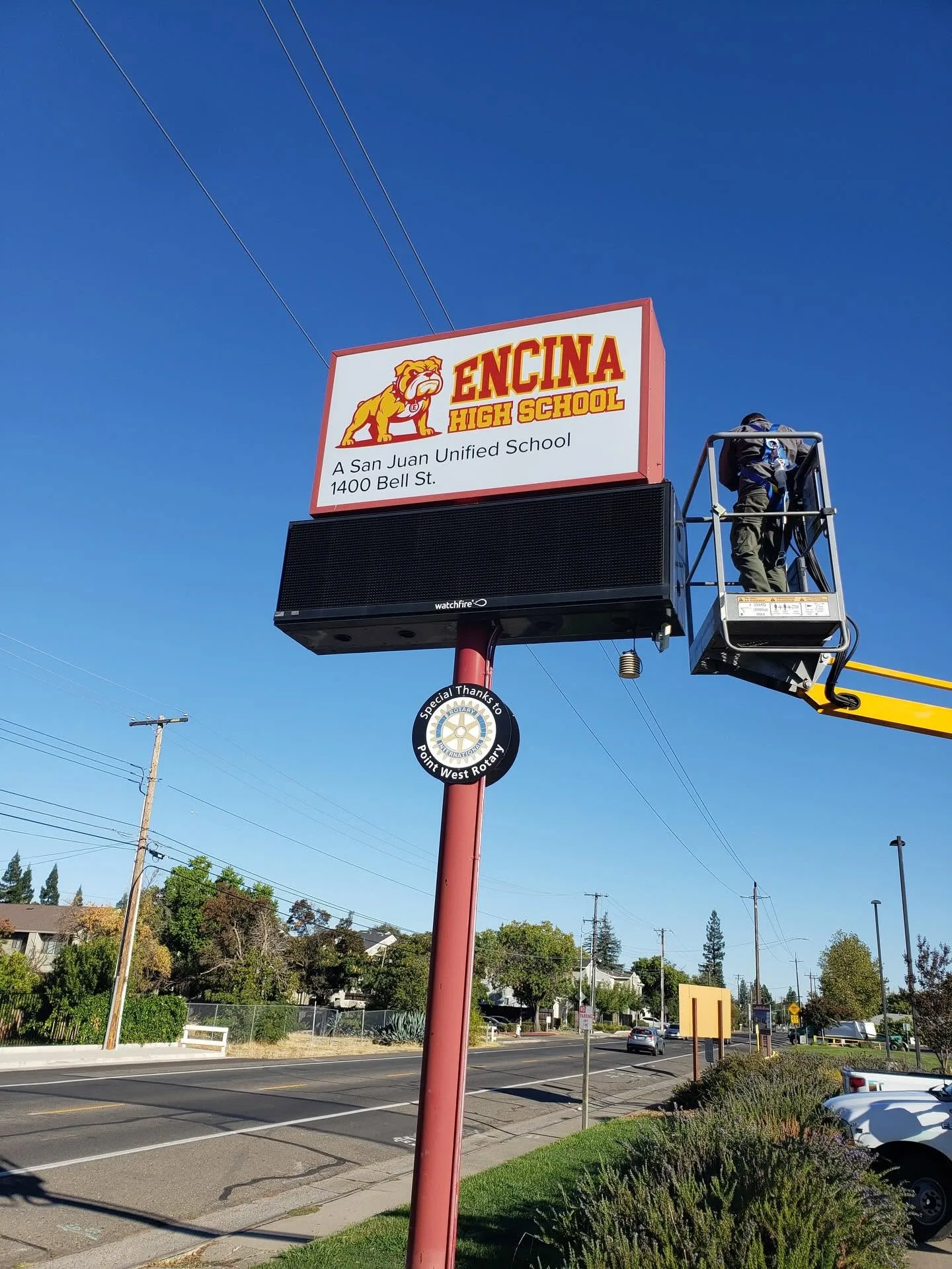 Worker in a boom lift installing a lighted pole-mounted school sign with bulldog mascot and LED reader board at Encina High School under a
