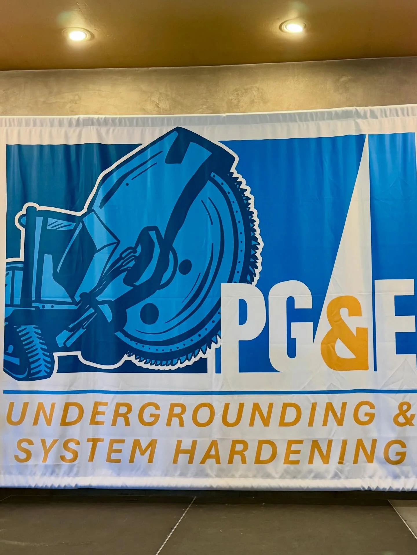Large wide-format fabric backdrop banner for PG&E Undergrounding & System Hardening with a blue trenching-machine illustration, hung