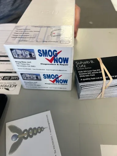 Shrink-wrapped boxes and banded stacks of printed business cards on a counter, including cards for Smog Now LLC (Sacramento) and Suhaib B.