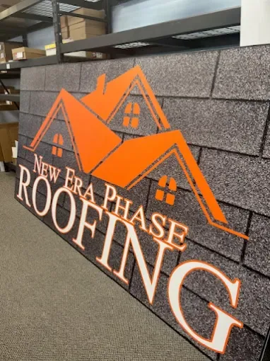 Large printed sign panel with a shingle-texture background and orange roof graphic for New Era Phase Roofing, leaning against shelving in