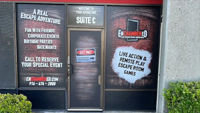 Storefront entrance of Enchambered Suite C with full window and door wraps in a brick theme listing event offerings, website, and phone